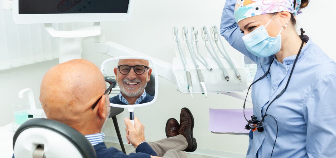 man smiling in a mirror, happy with his tooth implants