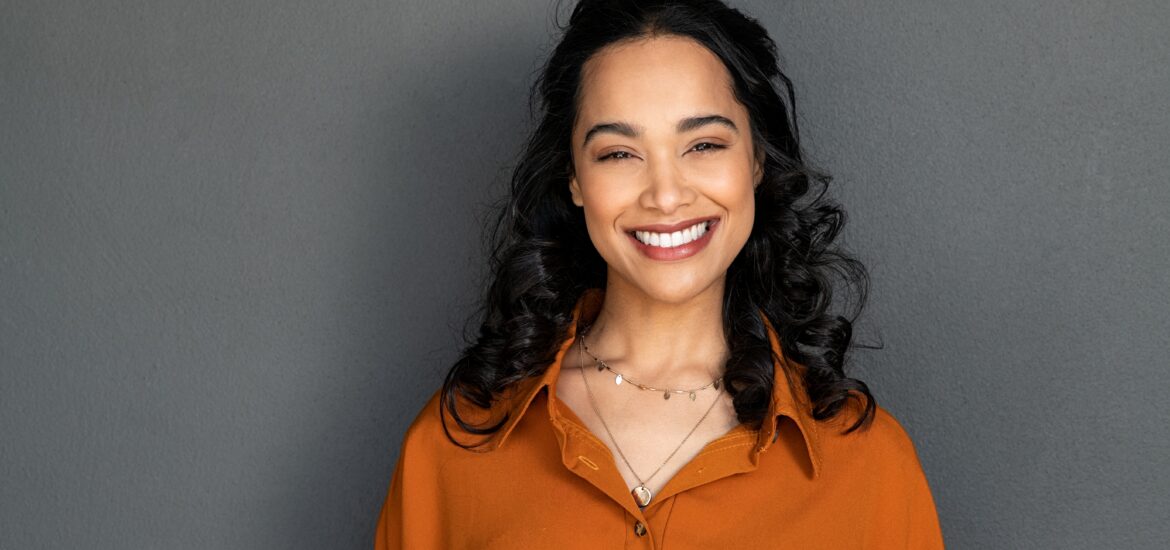 dark haired woman smiling against a grey backdrop, perfect teeth