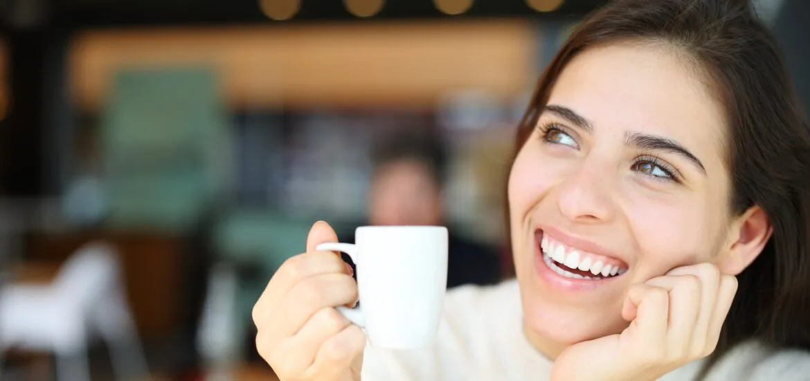 Happy woman with perfect teeth dreaming and drinking coffee in a restaurant