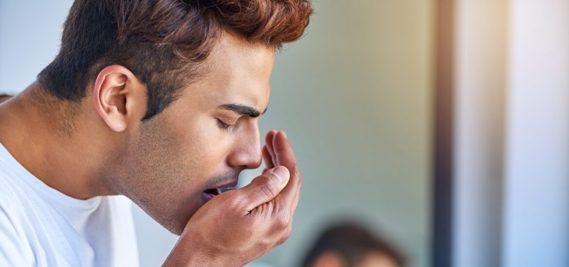 man blowing into his hand checking his breath in the mirror