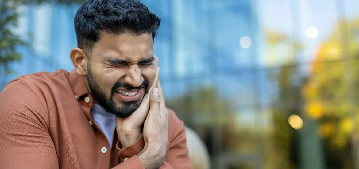 An indian man is experiencing a severe toothache, he is holding his face in pain and discomfort.