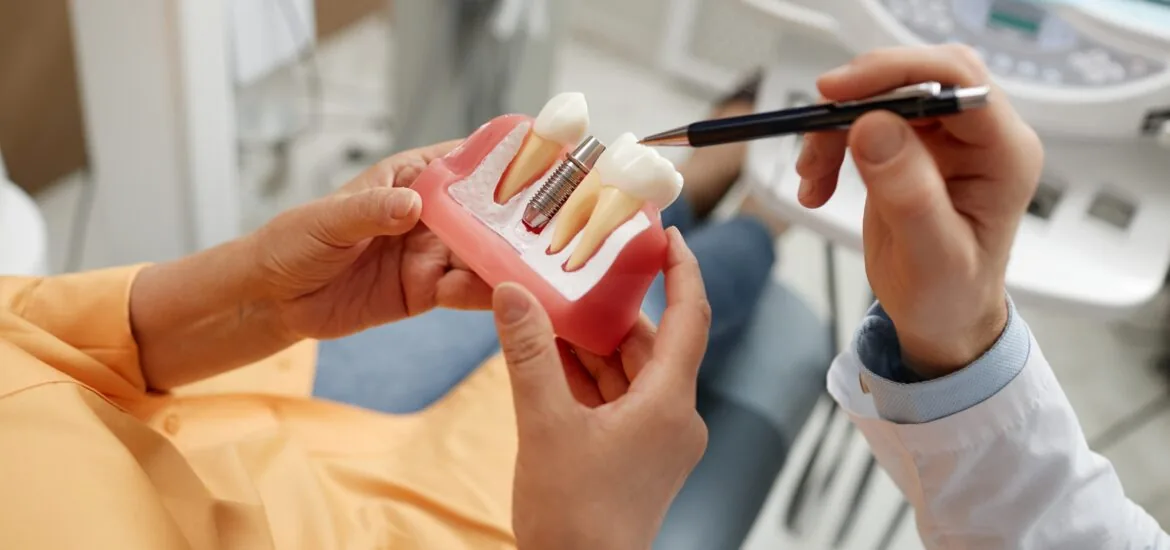 dentist showing a patient in an orange shirt a dental implant model